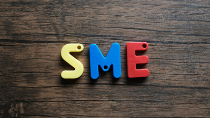 Word 'SME' from wooden letters on dark wooden background