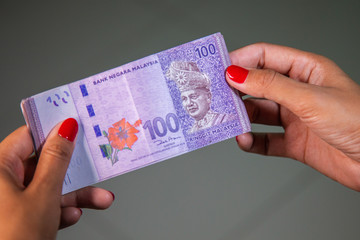 Female Hands with red nails counting 100 Ringgit banknotes. Ringgit the currency of Malaysia. Woman hands showing RM100 notes. Close up to the Malaysian money with colorful fingernails 