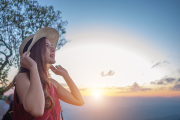 Smiling woman traveler in mountains at sunset holding hat and looking at view of nature chiangmai landmark in thailand with backpack in holiday, relaxation concept, travel concept