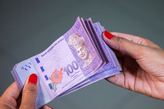 Female Hands with red nails counting 100 Ringgit banknotes. Ringgit the currency of Malaysia. Woman hands showing RM100 notes. Close up to the Malaysian money with colorful fingernails 