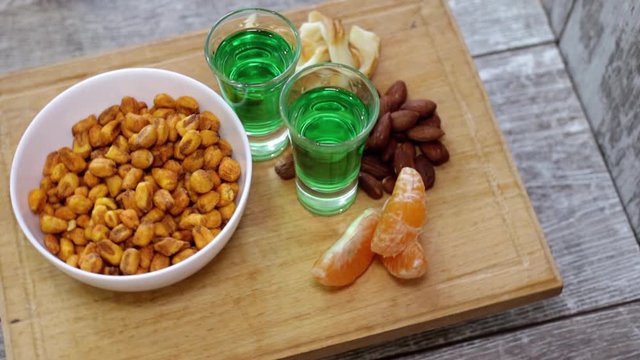 Two shots with green absinthe and different appetizers rotate on a wooden stand
