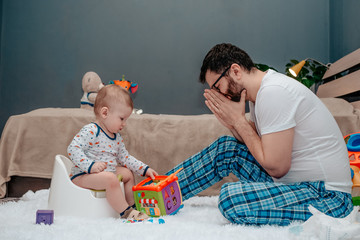 Father and son. Father teaches a child to walk on a potty. Father makes an appealing gesture with his hands. Dad is tired of waiting. The child is playing. Baby toiletries. Potty training.