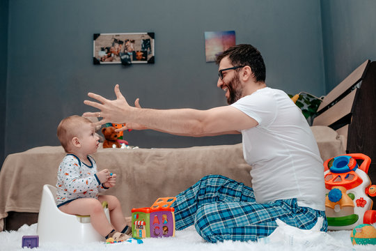 Father And Son. Father Teaches A Child To Walk On A Potty. The Father Is Happy And Ready To Hug The Child. Dad Is Very Happy About The Success Of His Son. Baby Toiletries. Potty Training.