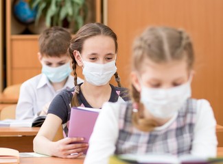 Schoolkids with medicine mask on faces against virus or flu in classroom