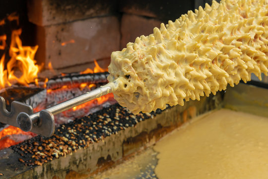  on the street at the wood stove are preparing Lithuanian tree cake, known as raguolis (which means "spiked") or sakotis