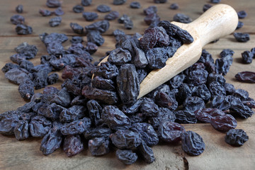 black raisins in a scoop on a wooden table. heap of black raisins close up
