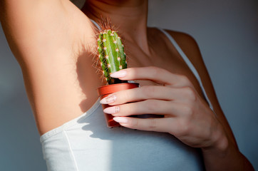 Obraz premium Woman's hand holding green cactus near her armpit,Depilation concept. Body positive concept. Concept of not shaving.