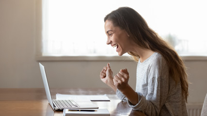 Excited young woman triumph reading good news online