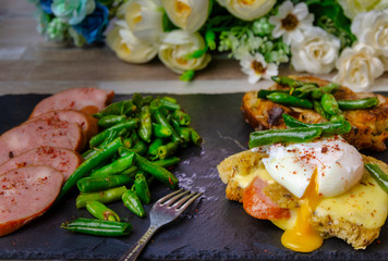 Breakfast on a black slate blackboard. Croutons with cheese, sausage, poached egg, green green beans.