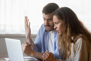 Frustrated millennial couple shocked having problems with laptop
