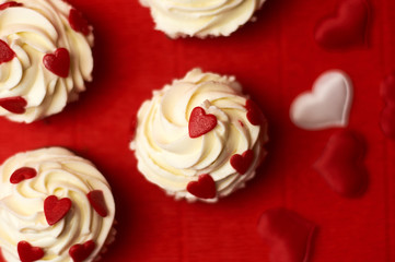  custard cakes decorated with hearts on a red background, top view.