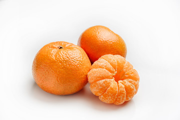 Tangerines on a white background. One peeled tangerine lies next to two tangerines in a peel.