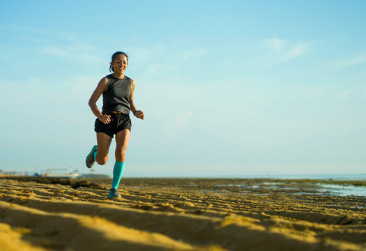 outdoors fitness portrait of young attractive and happy Asian Indonesian woman in compression socks jogging cheerful on the beach doing running workout