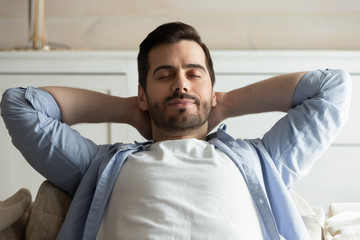 Obraz premium Calm millennial man relaxing with eyes closed on cozy couch