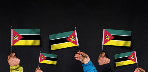 Hands holds flags of Mozambique on dark background