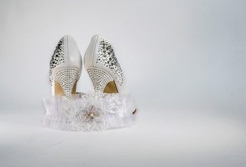 The bride's white shoes. Beautiful garter, champagne glasses and beige roses for the wedding ceremony.