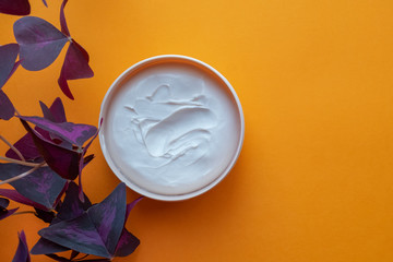 Open jar with face cream or body and leaf of homemade plant oxalis on an orange background.