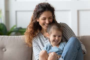 Laughing curly mom embracing little child girl.