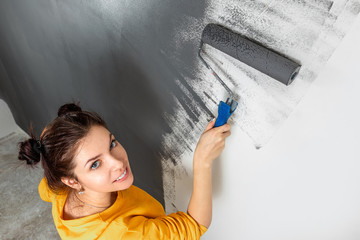 Beautiful young girl paints a wall in a yellow jacket with a roller, gray paint. The concept of repair, change, design, interior.