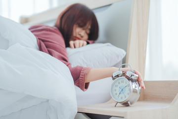 Waking up in the morning on time,alarm clock standing on bedside table going to ring early morning to wake up woman in bed sleeping in background