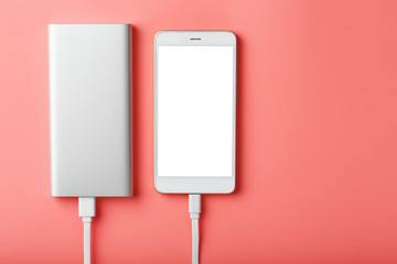 Powerbank charges a smartphone on a pink background. Universal external battery for gadgets Free space and minimalistic composition.