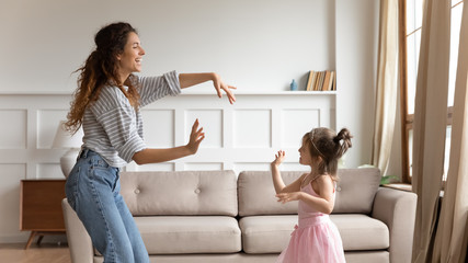 Young babysitter dancing to music with daughter at home.