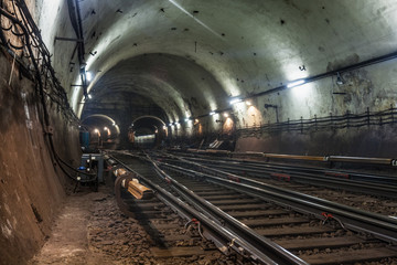 Obraz premium Lighted white reinforced concrete subway tunnel. With railway interchange, track development. Passing train. Arriving at the station by train. Cable routes laid on the walls of the tunnel