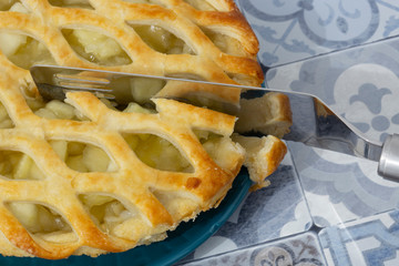 Bramley apple pie with lattice pastry topping being sliced with a cake cutter on a blue platre. Blue tile background