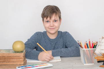 Back to school. A beautiful boy of 10 years old student of the 3rd grade draws drawings on a table...