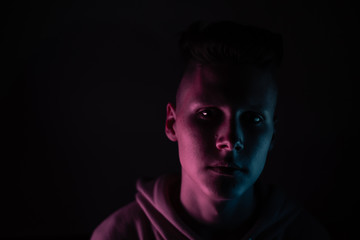 Young guy in a neon light. A teenager in a pink hoodie in trendy lighting of pink, purple and blue. Copyspace