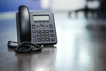 Close Up Black ip phone is placed on a wooden floor in the office.