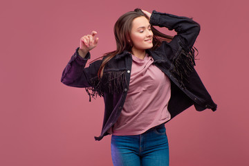 cheerful girl in a fringed jacket dances on a pink background.
