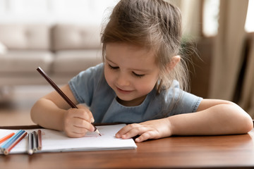 Cute little preschool child girl drawing pictures with colored pencils.