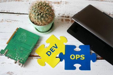 puzzle with Dev and Ops words near laptop and motherboard. DevOps Concept for software engineering...