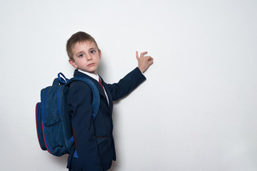 Serious schoolboy in school uniform with backpack writes on the blackboard. Half-length portrait, white background. Copy space