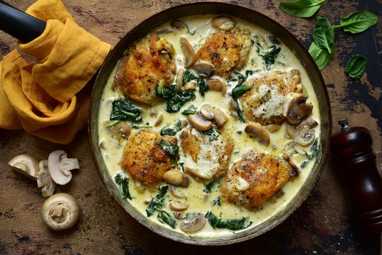 Chicken thighs stewed with mushrooms and spinach in a cream sauce. Top view with copy space.