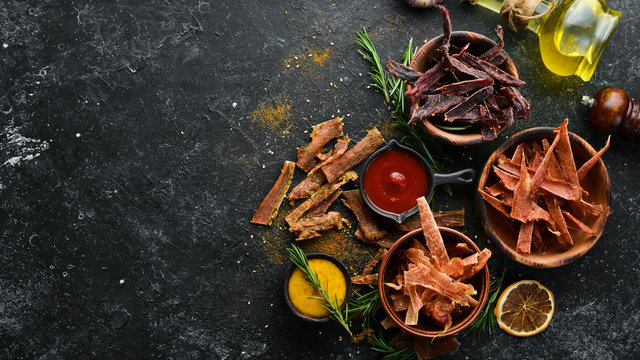 Jerky. Dried meat slices with spices and herbs. Snacks for beer On a black stone background. Top view.