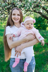 Fototapeta premium Young mother with little daughter on hands over nature background. Vertical frame