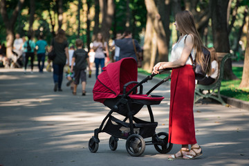 Young mother walking in the Park with a pram. Motherhood pfrenthood concept