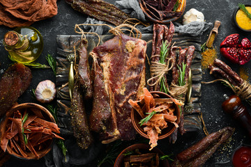Jerky, dried veal, salted pork and rosemary smoked sausages. Snacks for beer On a black stone...