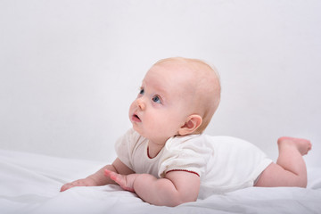 Cute and curious baby. Newborn lays on his stomach on bed. Side view