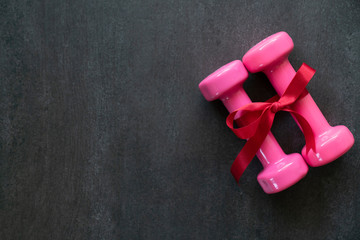 two dumbbells with red gift bow on a black table background, sport and healthy concep