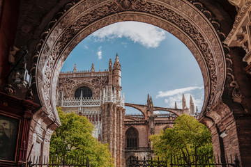 Naklejka premium Piękno katedry w Sewilli. Widok na północną fasadę katedry i dziedziniec pomarańczy przez bramę łukową. Największy gotycki kościół na świecie. Katedra Najświętszej Marii Panny, Andaluzja, Hiszpania, Europa