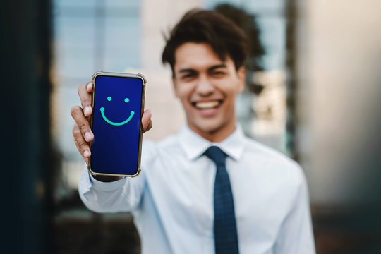 Customer Experiences Concept. Young Businessman Giving a Happy Face Icon and Positive Review via Smartphone. Client's Satisfaction Surveys on Mobile Phone. Front View