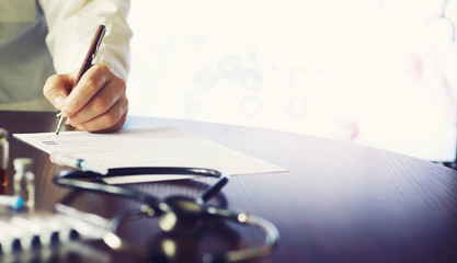 A man signs a medical document. Medical equipment on the table. Stethoscope and ampoules with syringes. Makes notes in the office. Medical center.
