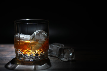 A glass of strong alcoholic drink with ice on a wooden bar counter. Whiskey with ice cubes. Glass with a chilled drink.