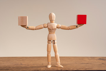 Wooden man extended his arms in different directions, hold two cubes, red and white. Copy space for...