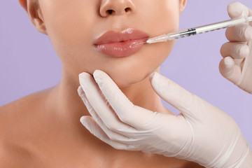 Young woman getting lips injection on lilac background, closeup