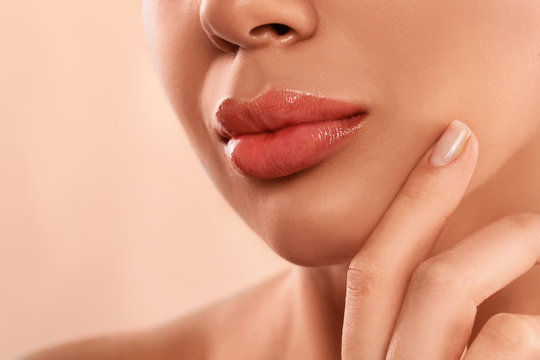 Young woman with beautiful full lips on peach background, closeup