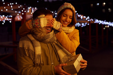 Woman presenting gift to her boyfriend at Christmas fair. Happy couple